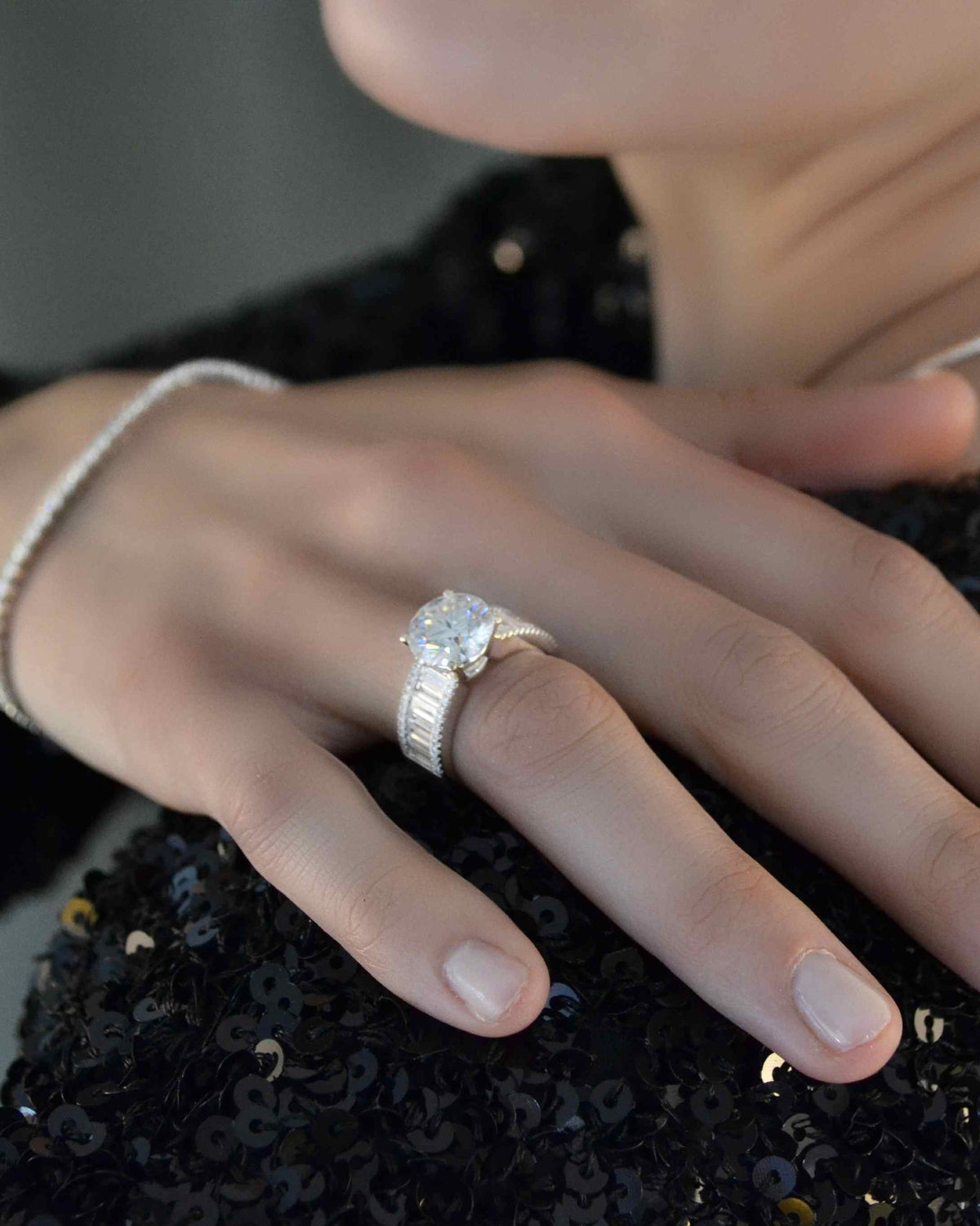 Hand with a diamond ring and bracelet on black sequins